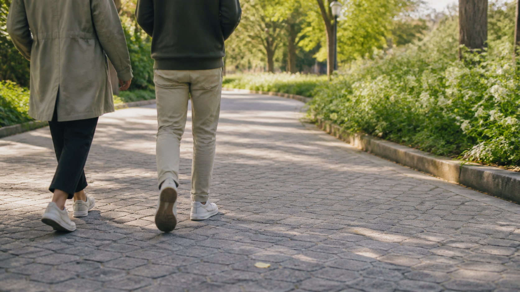 Two people walking side by side on a quiet sunlit path.